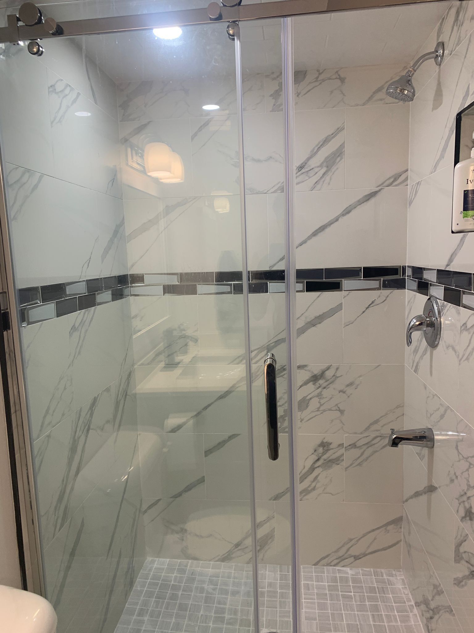 A glass-enclosed shower with a handheld showerhead and a wall-mounted faucet.