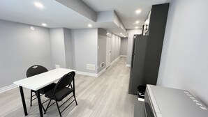 A modern kitchen with a white countertop, black chairs, and a grey refrigerator.