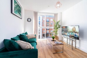 Un salon moderne avec un canapé vert, une table basse et un téléviseur diffusant un match.