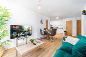 A modern living room with a TV, a dining area, and a kitchen in the background.
