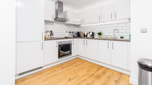 Una cocina moderna con armarios blancos, un horno de acero inoxidable y suelo de madera.