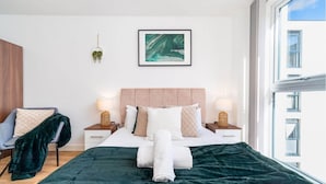 Una habitación de hotel con una cama, dos mesitas de noche, una silla, un ventanal y una planta en la pared.