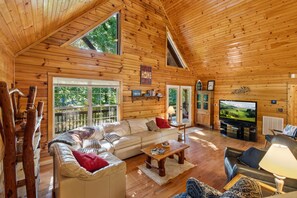 Ein Blockhaus-Interieur mit einer großen Couch, einem Fernseher und einem Kamin.