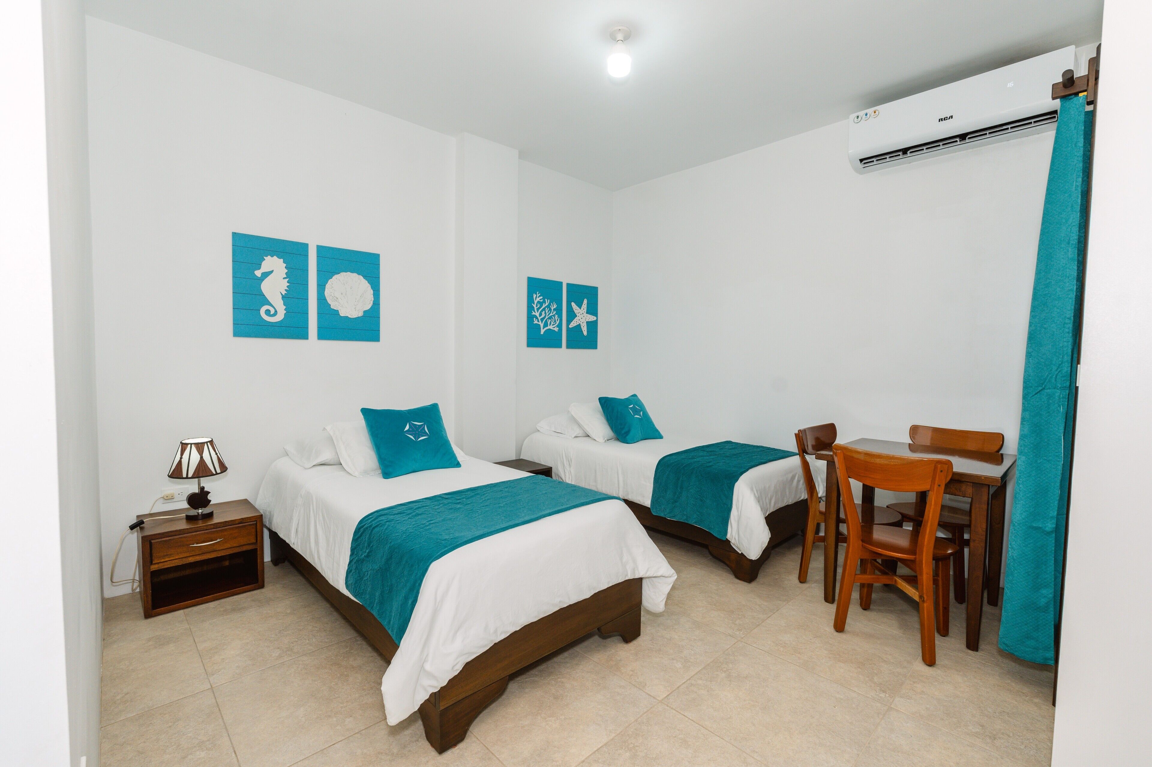 Habitación de hotel con dos camas, un escritorio y una silla. Incluye obras de arte en la pared y un equipo de aire acondicionado.
