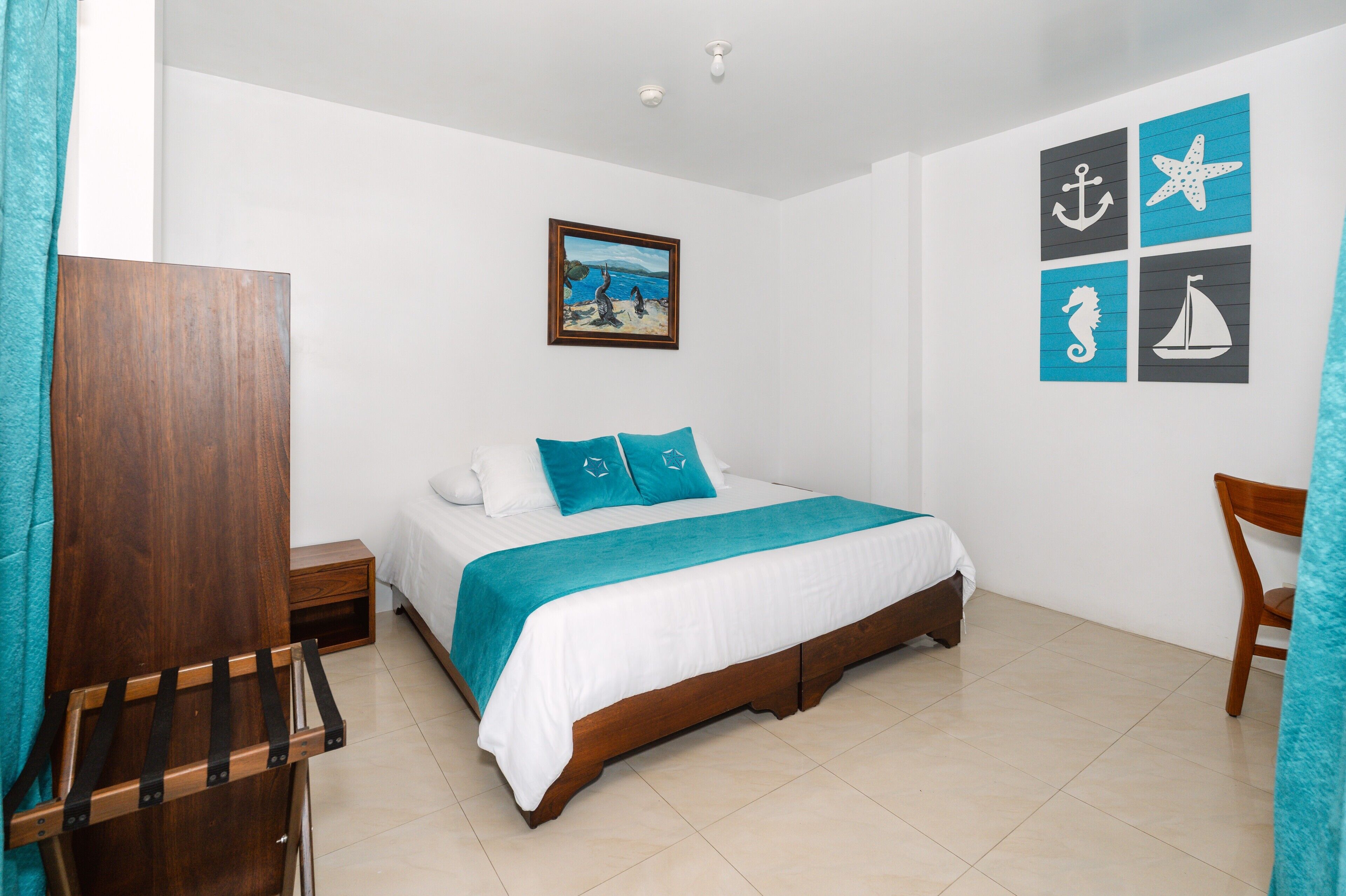 Un dormitorio con cama, mesita de noche, una silla de madera, un cuadro y decoración de temática náutica.