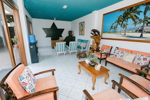 A room with a star wall decoration, a wooden reception desk, a painting of a beach, and a variety of seating options including chairs and a sofa. - Starfish Hotel (Puerto Villamil)