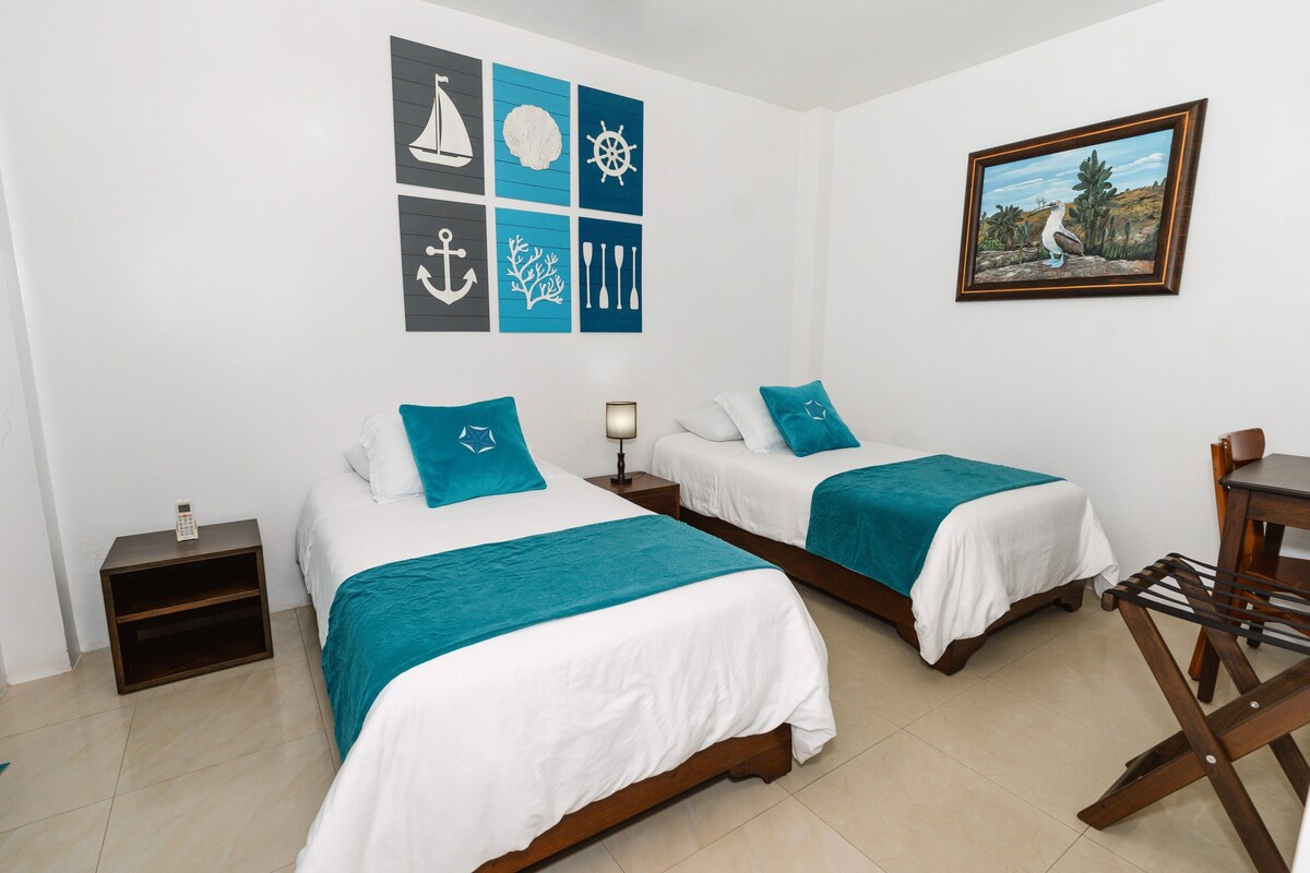 A hotel room with two beds, a small table, a chair, and a wall with nautical-themed decorations.