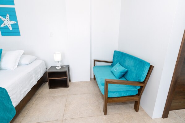 Una habitación con una cama, una mesita de noche, una lámpara y un sofá azul.