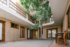 A spacious indoor area with a high ceiling, stone walls, and a large tree in the center. - Starfish Hotel (Puerto Villamil)