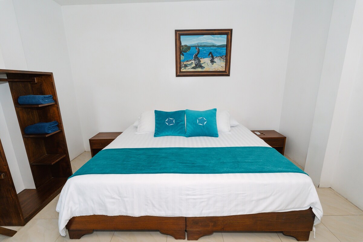 A bedroom with a bed, two nightstands, a wooden wardrobe, and a painting on the wall.