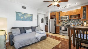 Un espacio habitable compacto con sofá, una pequeña cocina equipada con refrigerador, microondas y estufa, además de ventilador de techo.
