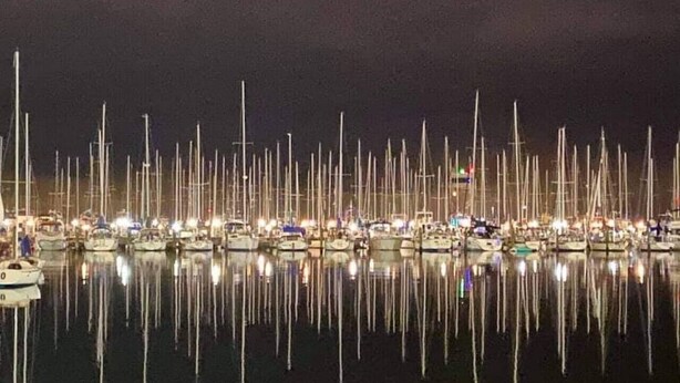 A marina with numerous boats docked at night, reflecting on the water.