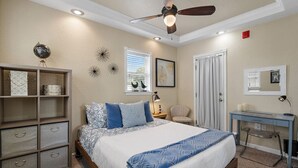 A bedroom with a bed, a desk, a chair, a globe on a shelf, and a ceiling fan.