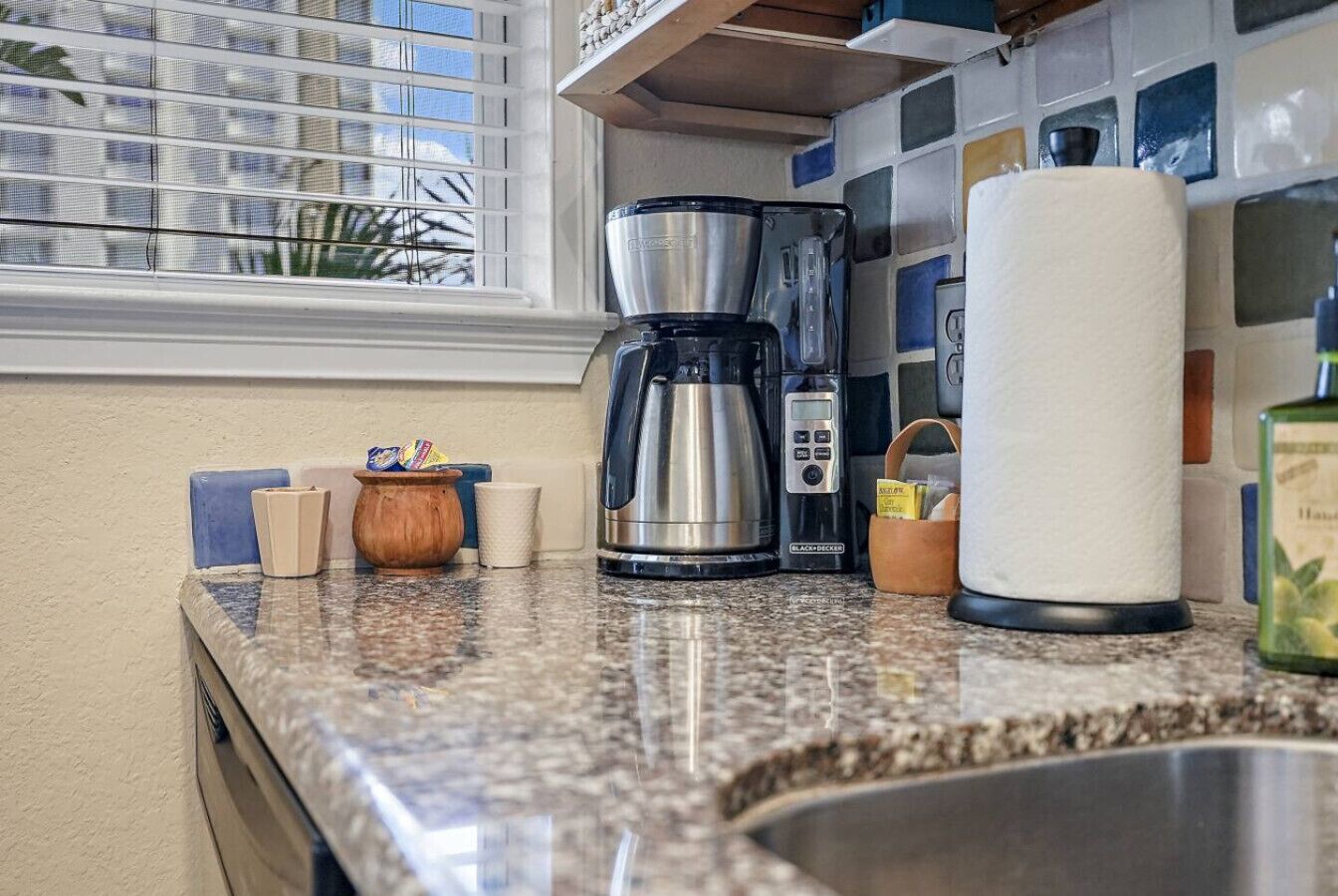 Una encimera de cocina con una cafetera, un dispensador de toallas de papel y una botella de aceite de oliva.