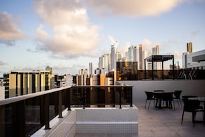 A rooftop terrace with a city skyline view, outdoor seating, and a glass balustrade. - Apart no Maradisa Design por Carpediem (João Pessoa)