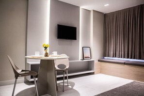 A modern room with a round table, two chairs, a flat-screen TV mounted on the wall, a window with curtains, and a small shelf with a picture frame. - Apart no Maradisa Design por Carpediem (João Pessoa)
