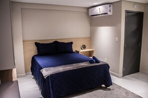 Un dormitorio con cama, mesita de noche, reloj y equipo de aire acondicionado.