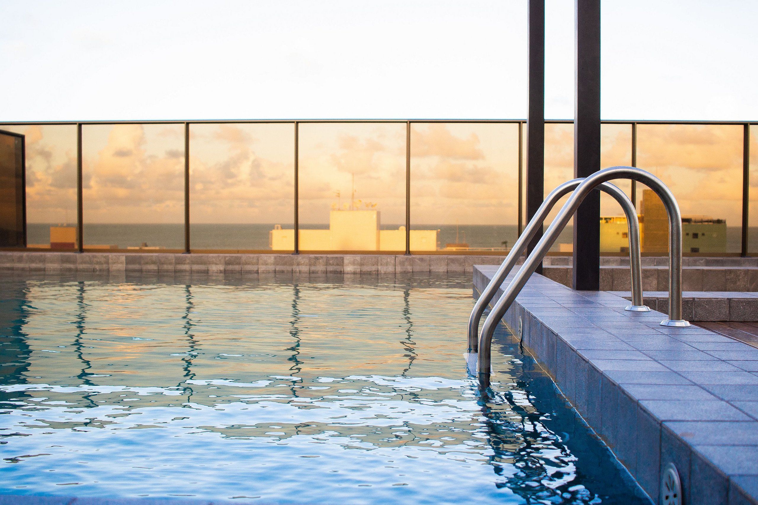 An indoor swimming pool with a view of the sea and buildings in the background.