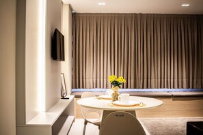 Un comedor moderno con una mesa redonda, sillas blancas, un jarrón con flores amarillas y un televisor montado en la pared.