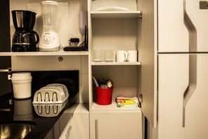 Una kitchenette con cafetera, licuadora y refrigerador pequeño.