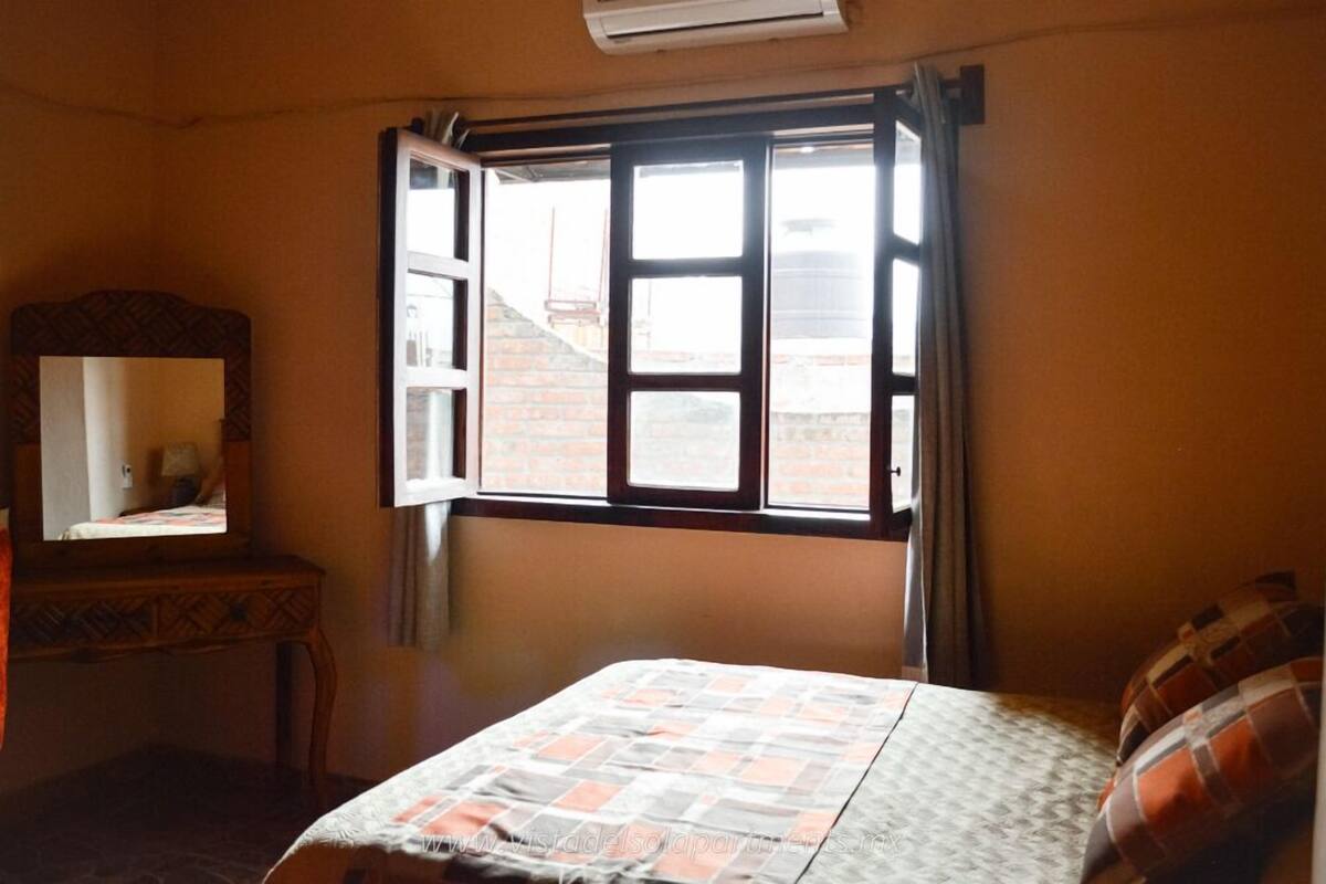 Une chambre à coucher avec un lit, une commode et une fenêtre dont le volet est ouvert.
