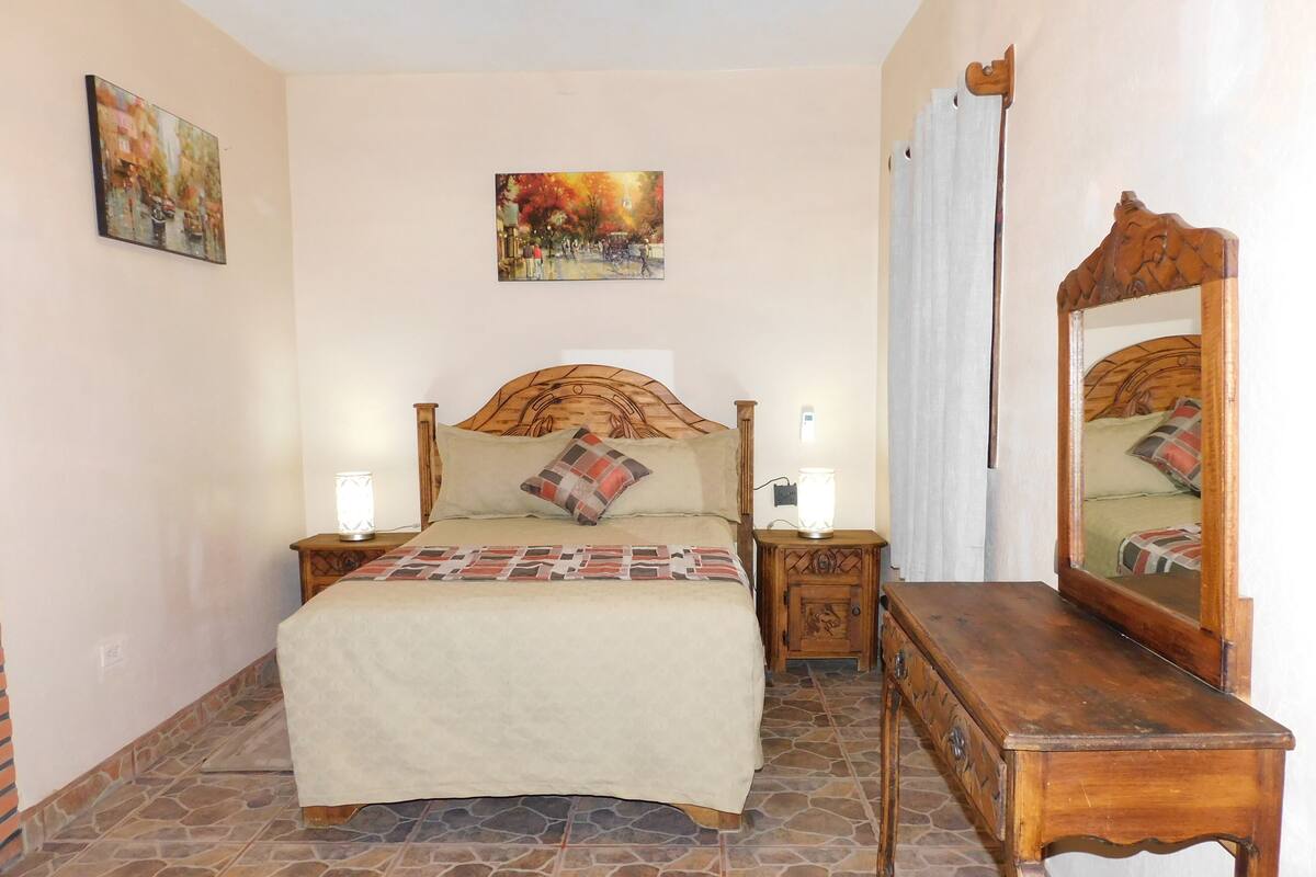 Une chambre à coucher avec un lit, des tables de chevet, un miroir et des œuvres d’art accrochées aux murs.