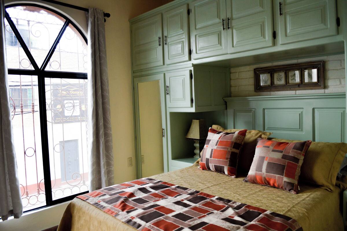 Une chambre à coucher avec un lit, des oreillers, une fenêtre avec des rideaux et des meubles de couleur vert clair.