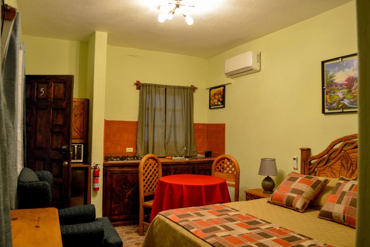 Une chambre à coucher avec un lit, une petite table, une chaise, un bureau et une fenêtre avec des rideaux.