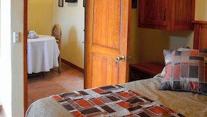 A bedroom with a bed, wooden cabinets, a table with a chair, and a door leading to another room. - Vista Del Sol Apartments (San Miguel de Allende)