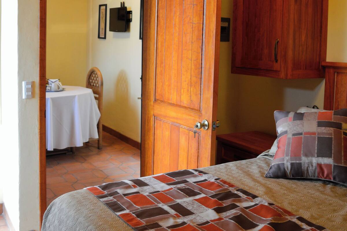 Une chambre à coucher comprenant un lit, des armoires en bois, une table avec une chaise et une porte donnant sur une autre pièce.