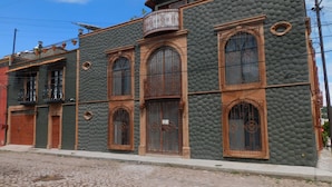 A building with a textured facade, large arched windows, and a balcony with wrought iron railings. - Vista Del Sol Apartments (San Miguel de Allende)