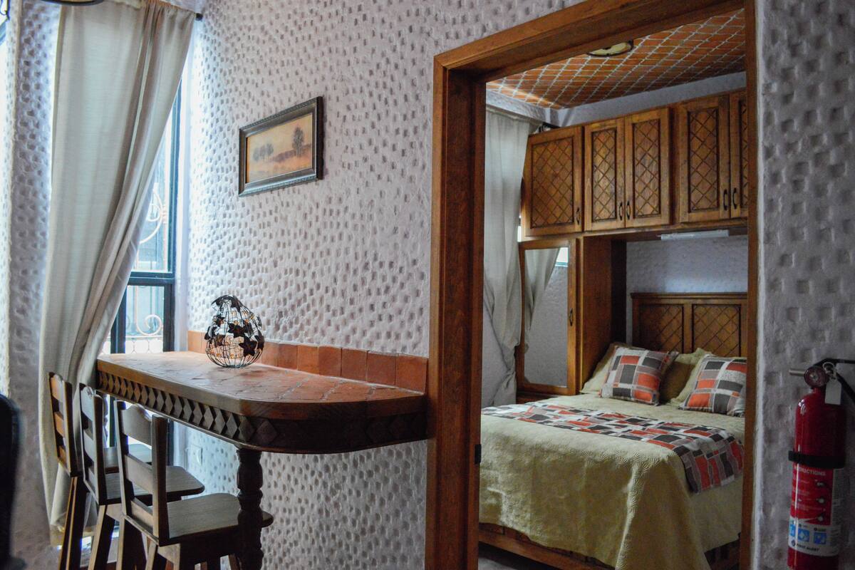 Une pièce avec une table en bois, des chaises, un lit avec une couette et un extincteur.