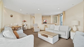 A modern living room with a sofa, armchairs, a coffee table, and a dining area with a table and chairs.