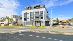 A modern multi-story building with balconies, a gated entrance, and a clear sky.