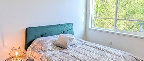 A bedroom with a bed, a ceiling fan, a window, and a nightstand with a lamp.