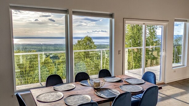 A dining area with a large table, chairs, and a view of the landscape through large windows. - Beautiful Modern Loft | Denali Views, Pool Table, Roof Deck, Firepit (Anchorage)