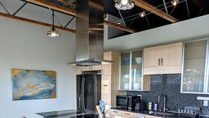 A modern kitchen with a central island, bar stools, stainless steel appliances, and a large window. - Beautiful Modern Loft | Denali Views, Pool Table, Roof Deck, Firepit (Anchorage)