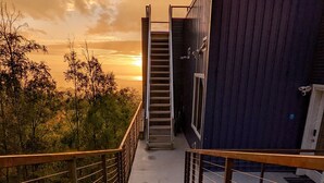 A metal staircase leading to a building with a view of trees and a sunset. - Beautiful Modern Loft | Denali Views, Pool Table, Roof Deck, Firepit (Anchorage)