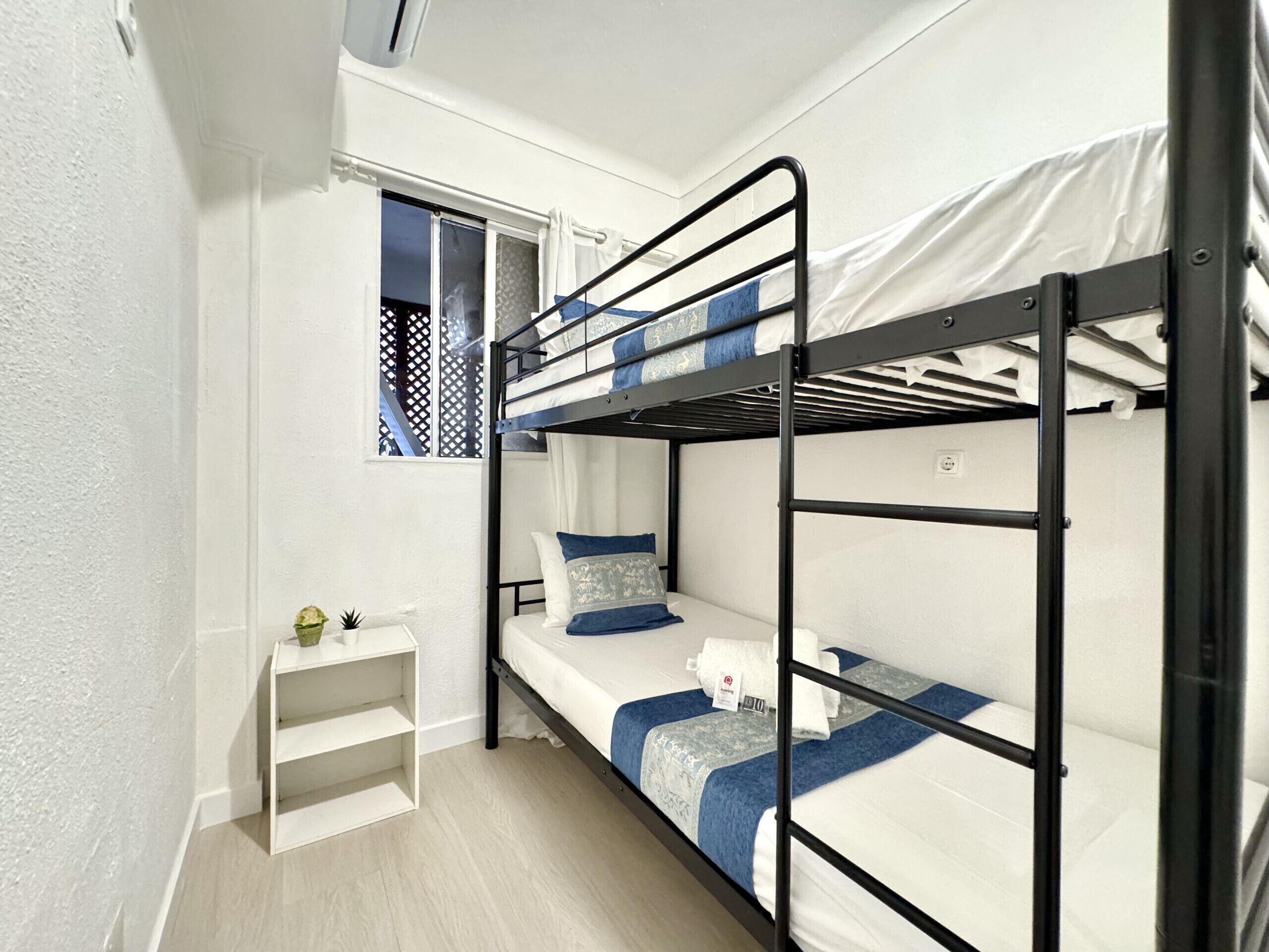 Habitación con literas, una pequeña estantería y una ventana con diseño de celosía.