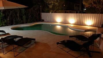 Una piscina con cubierta de madera y sillas de descanso, rodeada por una valla de madera y árboles.