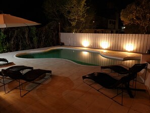 A swimming pool with a wooden deck and lounge chairs, surrounded by a wooden fence and trees.