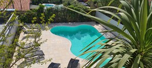 A swimming pool with a curved edge, surrounded by a tiled deck and a white fence.