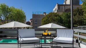 A deck with two white cushioned chairs, a small table with drinks, and a pool in the background. - Hotel Arte del Rey (Pinamar)