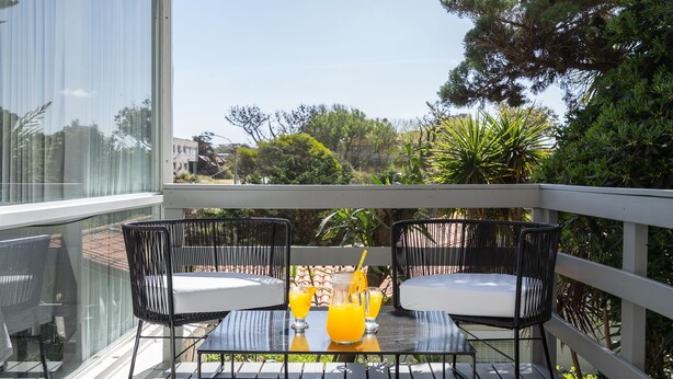 A balcony with two black wicker chairs, a glass table, and three glasses of orange juice. - Hotel Arte del Rey (Pinamar)