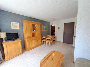 Una habitación con un armario de madera, un televisor, una mesa de comedor con sillas y una puerta.