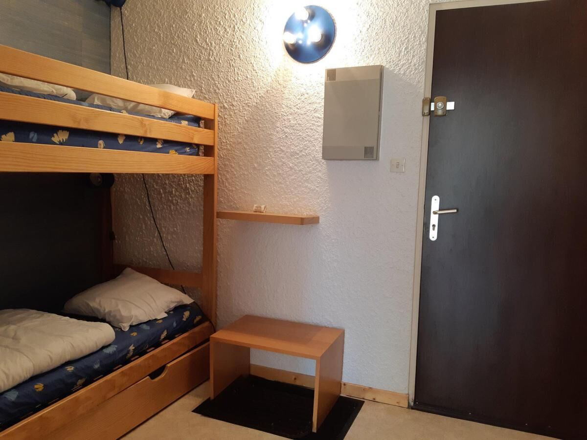 Een kamer met een stapelbed, een klein houten tafeltje, een wandlamp en een deur.