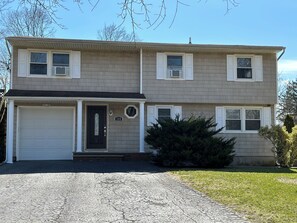 A two-story house with a garage, a front door, and a mailbox. - fully Modern 3 bedroom 65"smart tvs cable bluetooth speakers etc (Islip)