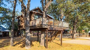 Una caseta d'arbòria de fusta amb un balcó, envoltada d'arbres.