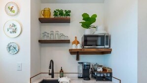 Una cuina petita amb un rentaplat, armaris de fusta, un refrigerador negre i un microones a la prestatgeria.