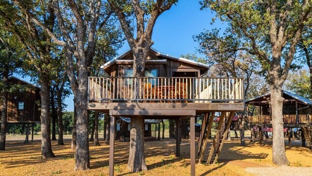 Una cabana de fusta amb un balcó, envoltada d'arbres.